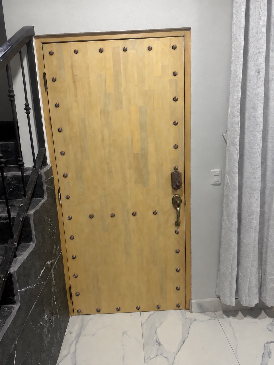 Wood entry door with decorative metal studs beside the staircase