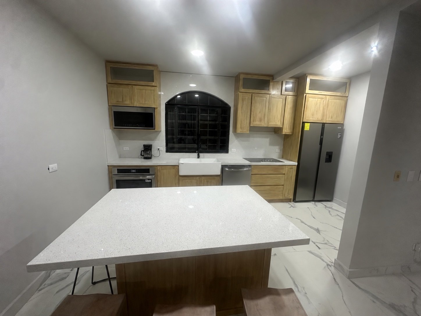 Front view of the remodeled kitchen with island, farmhouse sink, cabinetry, and appliances
